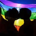 Dois jovens se beijam sob a bandeira LGBTI+, simbolizando o orgulho LGBTI+ como resistência e afeto em um país que ainda nega direitos e dignidade.